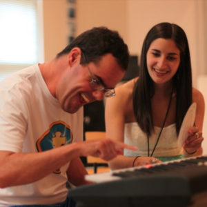 A music therapist working with a individual on the keyboard.