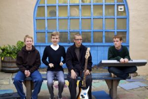 A group of kids sitting on a bench holding several music instruments.