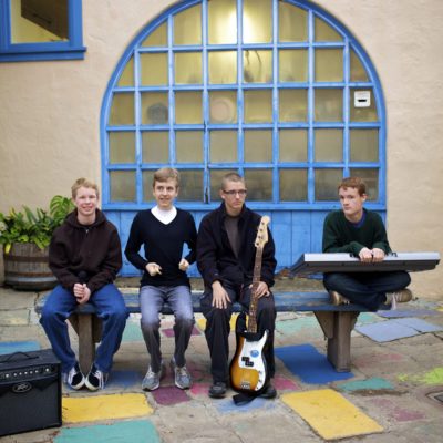 A group of kids sitting on a bench holding several music instruments.